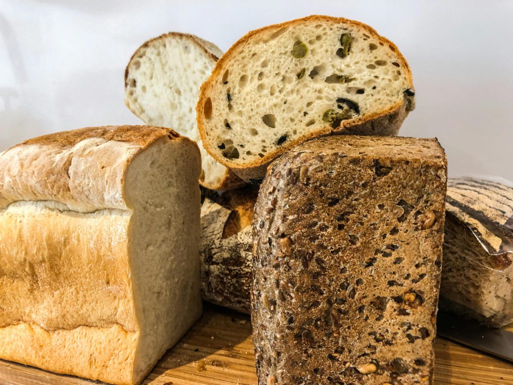 Close-up of various artisan bread loaves and slices on a wooden board, featuring fresh and baked textures.